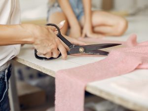 Mother with daughter at the factory. Family with a fabric. Woman use the scissors.