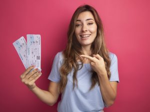 belle-jeune-femme-t-shirt-bleu-tenant-billets-avion-pointant-index-eux-souriant-joyeusement