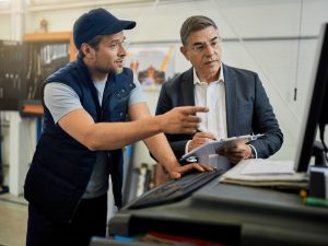mid-adult-manager-car-mechanic-talking-while-using-computer-auto-repair-shop (1)
